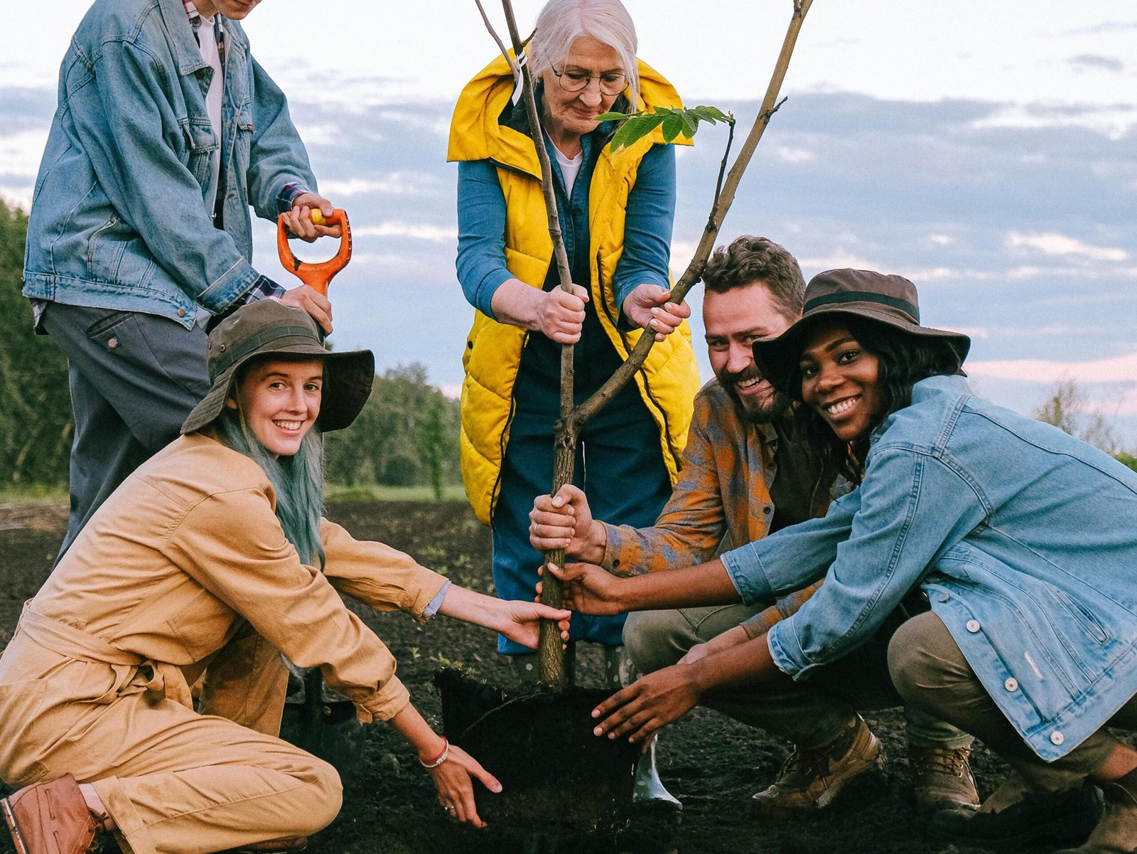 A joyful group of volunteers planting a tree outdoors, symbolizing community and teamwork.