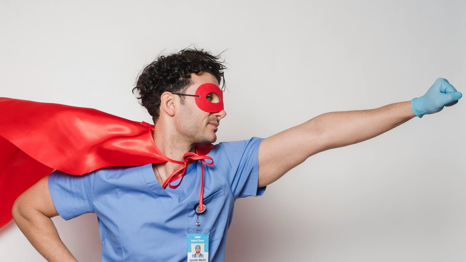 Male healthcare worker wearing a red cape and mask poses as a superhero. Studio shot.