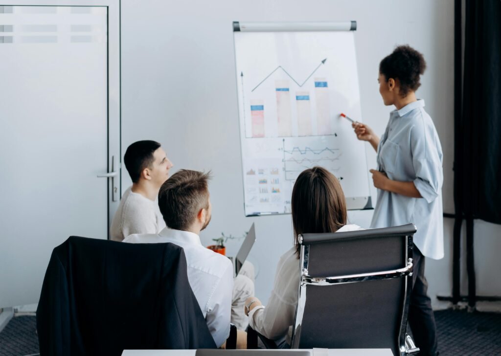 pexels-photo-6592684-6592684 Business team in meeting with presenter discussing charts on a flip board.