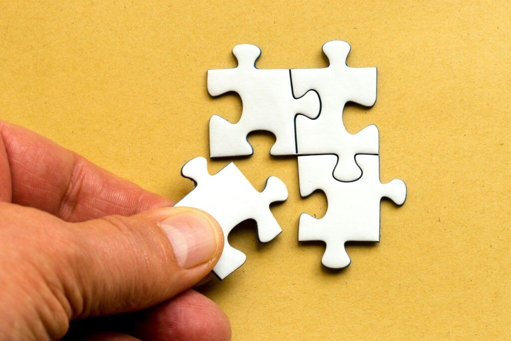pexels-photo-5505150-5505150 Close-up of a hand completing a white jigsaw puzzle on a yellow background.