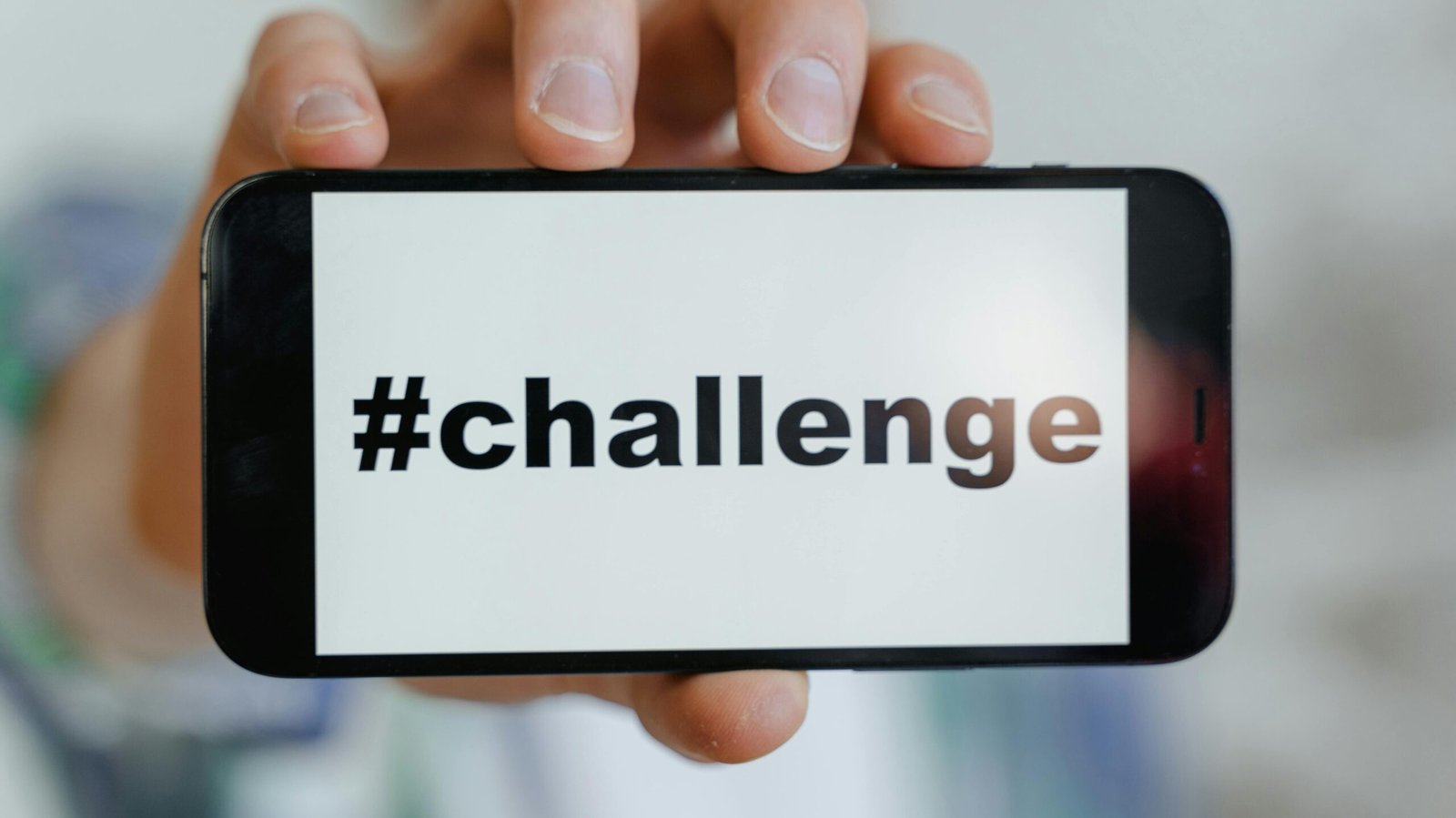 Close-up of a hand holding a smartphone displaying a '#challenge' hashtag.