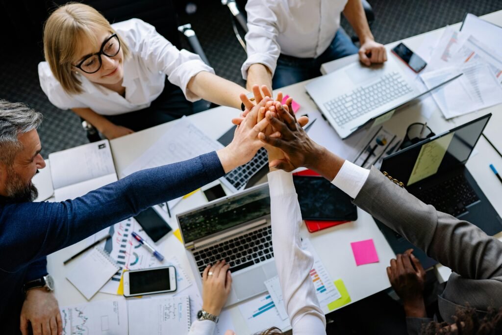 A group of diverse professionals high-fiving over a collaborative workspace.