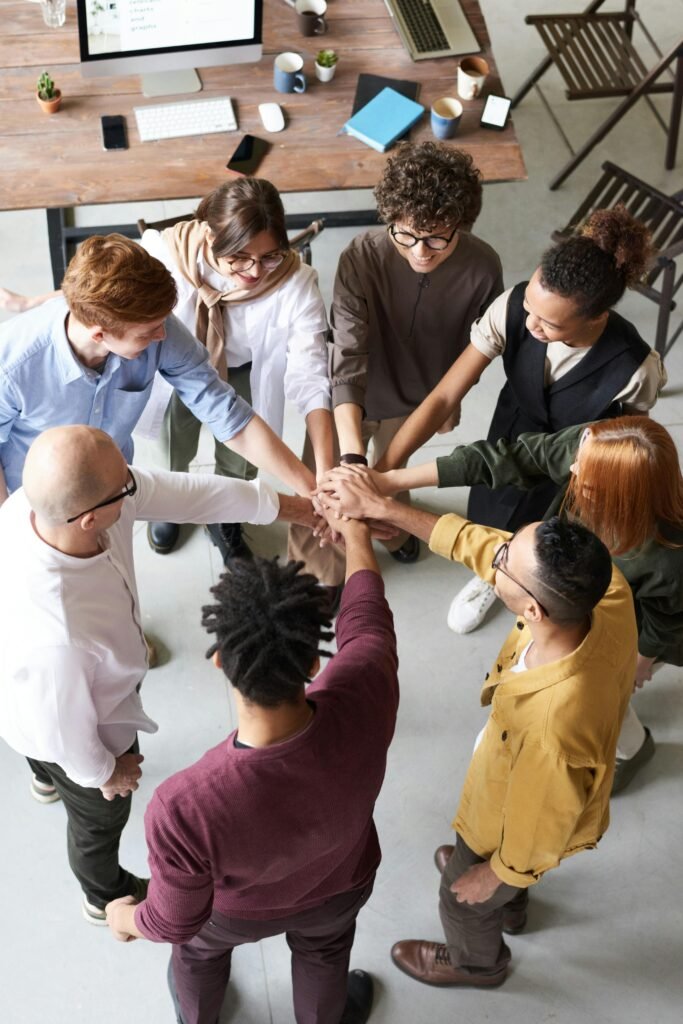 pexels-photo-3184423-3184423 A diverse group of professionals joins hands in a team-building exercise indoors.