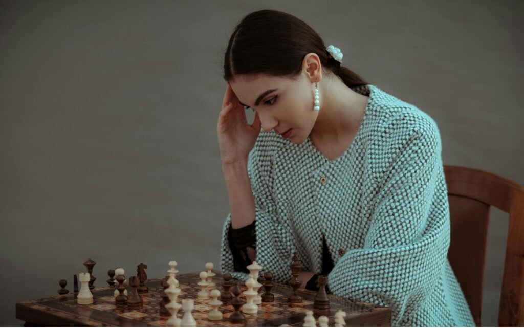 pexels-photo-7207270-7207270 Concentrated ethnic female sitting on chair and touching head while playing chess against blurred gray background