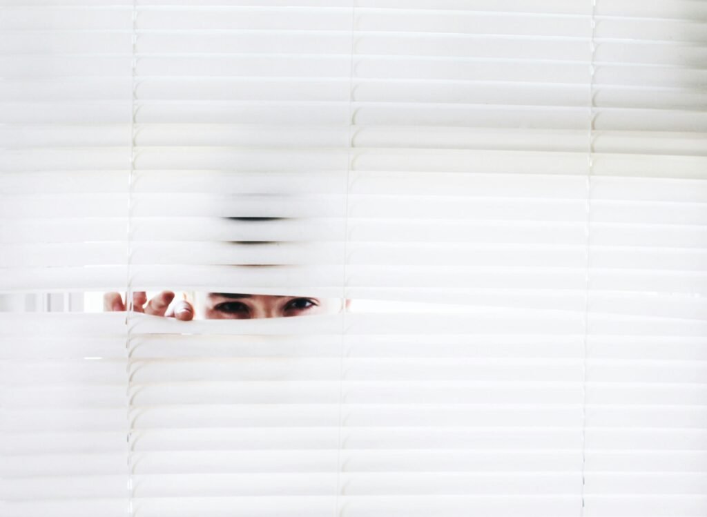 pexels-photo-906018-906018-1 A person peeks through white blinds, creating an intriguing sense of curiosity.