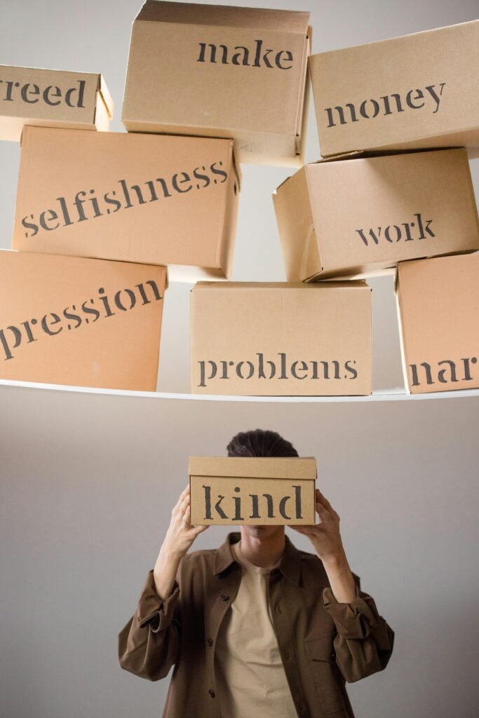 pexels-photo-9169318-9169318 A person holds a box labeled 'kind' amidst a backdrop of issues like greed and problems.