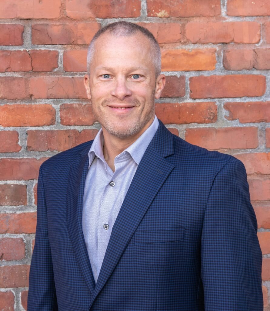 pexels-photo-14634935-14634935 Portrait of a professional man in a suit smiling against a rustic brick wall backdrop.