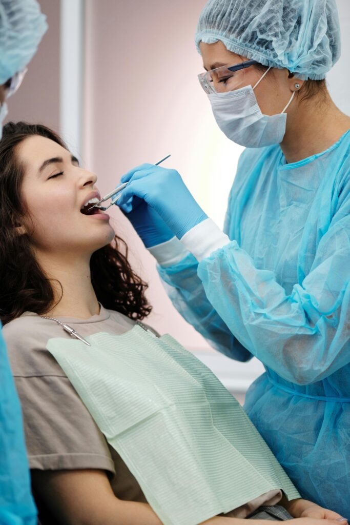 pexels-photo-4270362-4270362 Dentist in protective gear examining a woman's teeth during a dental clinic visit.