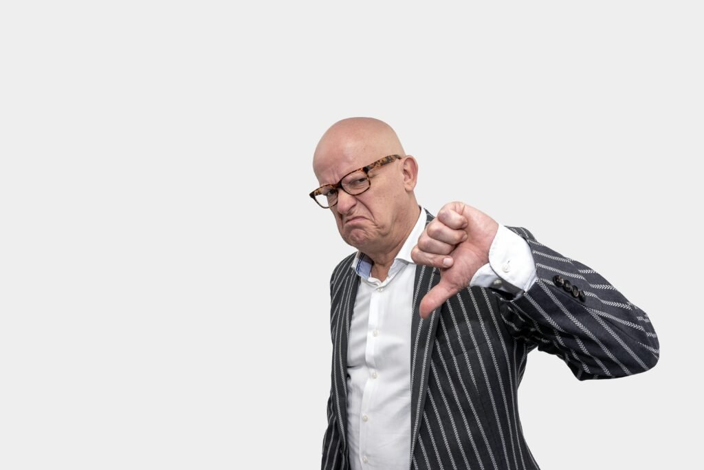 pexels-photo-5511613-5511613 Bald businessman in striped coat giving a thumbs down gesture against a white background.