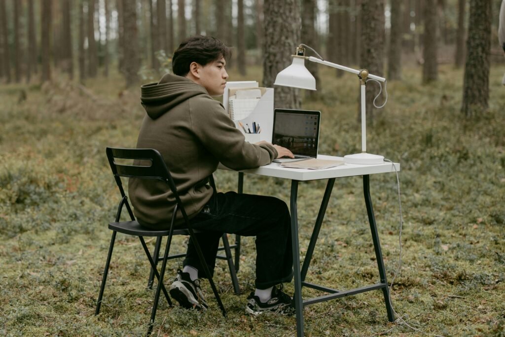 pexels-photo-6636101-6636101-1 Man working on laptop at an outdoor desk in a forest setting, embracing nature.
