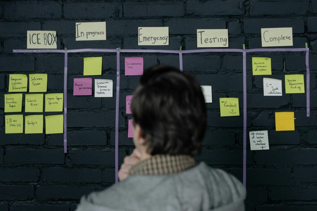 pexels-photo-6804077-6804077 A man in an office reviews a scrum task board filled with sticky notes, planning strategy and organization.