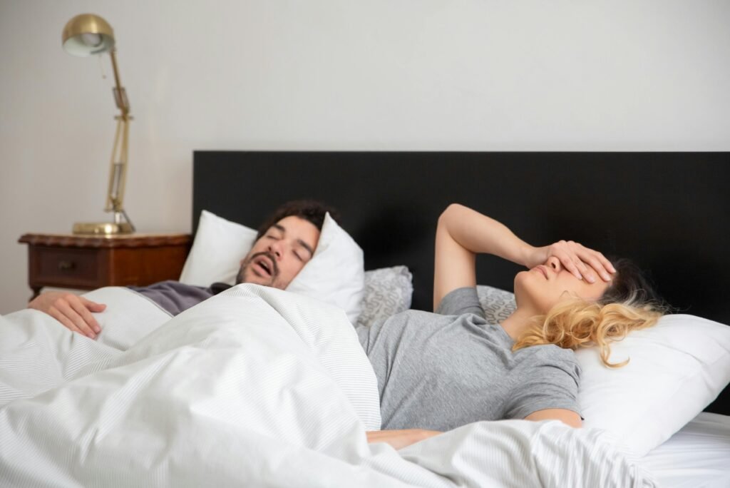 pexels-photo-7556565-7556565 A couple in bed, with one partner covering their face due to the other's snoring.