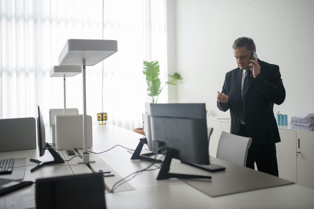 pexels-photo-8353770-8353770 Senior businessman in a black suit takes a call in a sunlit modern office space.