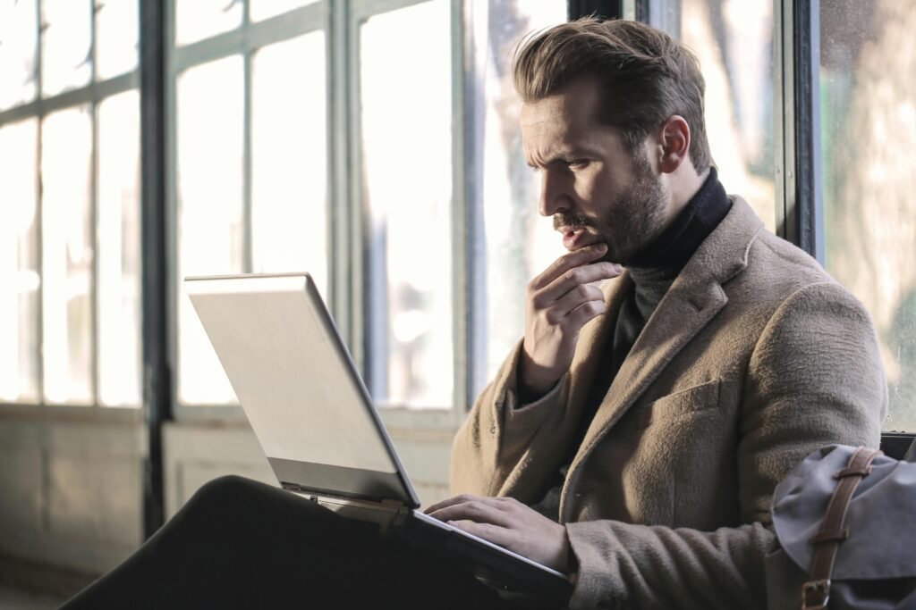 pexels-photo-874242-874242-1 Man looking contemplative while working on a laptop in a well-lit indoor space.