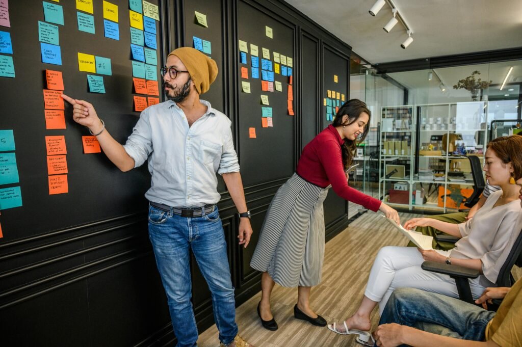 pexels-photo-4623478-4623478 Team members collaborating in a modern office with sticky notes on a wall, focusing on brainstorming and strategy.